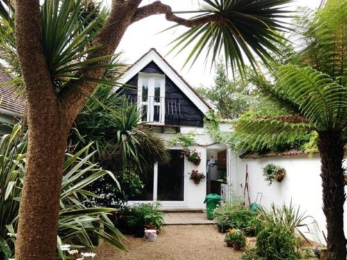 Two-storey UK home with newly painted exterior surrounded by trees and a colourful garden.