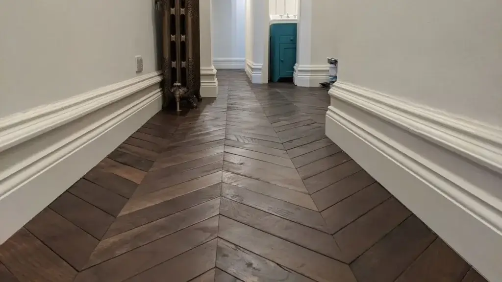 Wooden parquet flooring with a vintage-style white Victorian radiator, paired with white painted skirting and pale grey walls. skirting board paint calculator