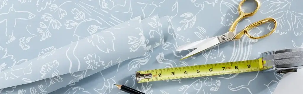 Wallpaper featuring a blue and white outline nature design, accompanied by a pair of shears, a tape measure, and a pencil, arranged on a flat surface.