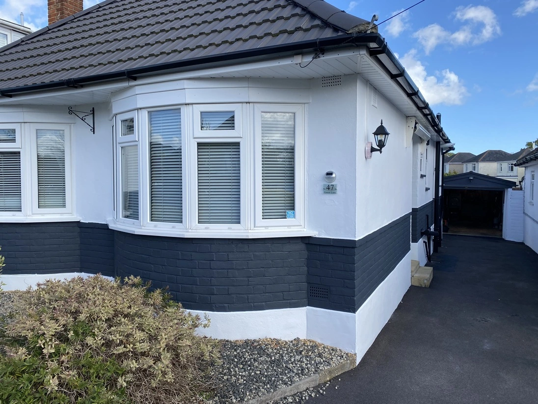 The front of a house with white painted walls and Anthracite painted brickwork and black painted pipes