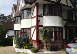 Exterior view of a beautifully renovated Tudor-style house with cream white walls, chocolate coloured wooden mock Tudor beams, and a well-maintained garden.