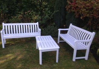 Outdoor setting with two newly painted Farrow and Ball white wooden garden benches and a matching white wooden table on a grassy lawn, surrounded by greenery